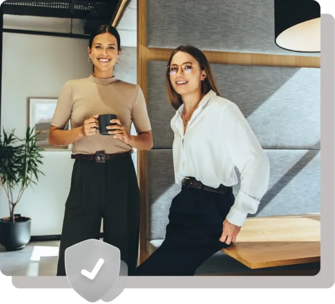 Two professional women smiling in a modern office lounge.