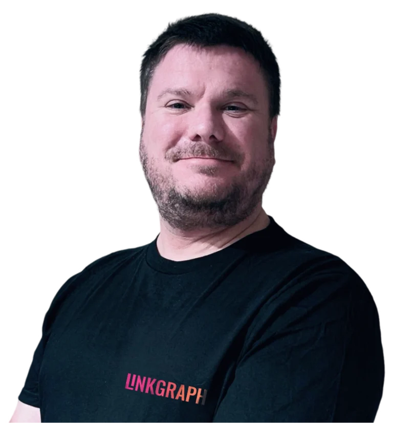 A man with short brown hair and a beard is standing with his arms crossed, wearing a black LinkGraph t-shirt.