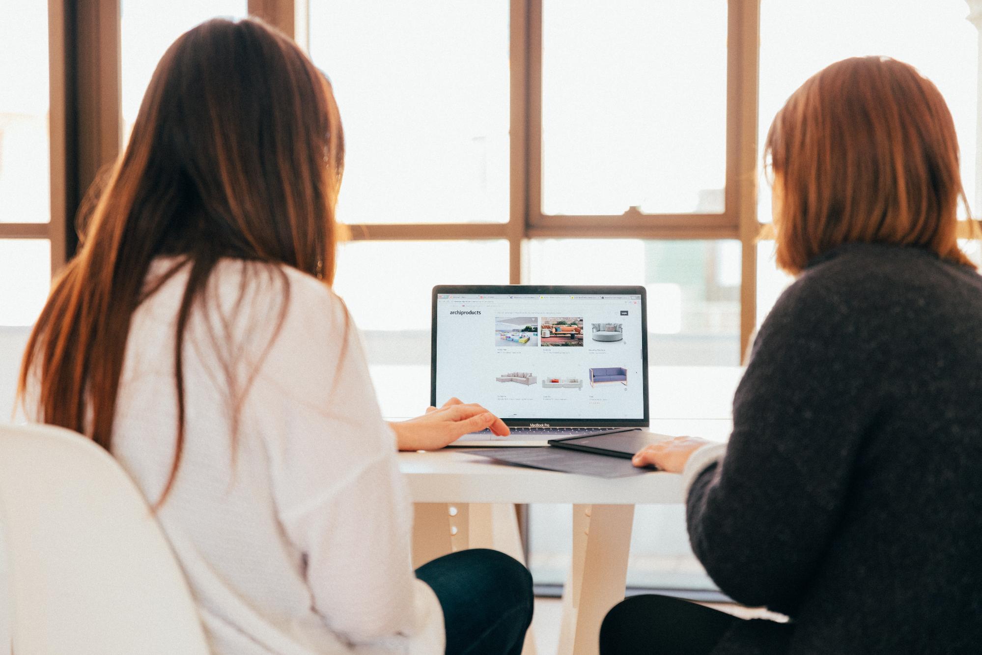 Two caucasian women sitting side by side with a laptop between, going through the customer journey