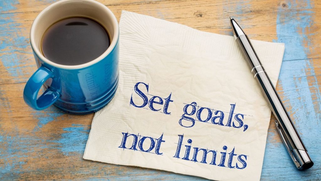 A coffee cup with Set goals, not limits image with a pen and napkin