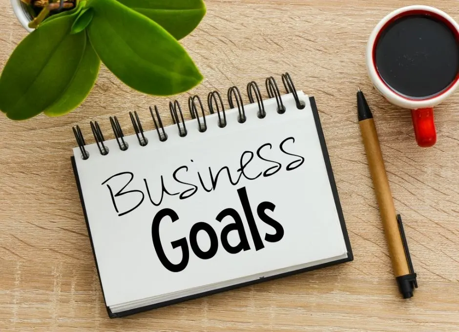 notebook with business goals written on it with a coffee mug, pen, and plant nearby