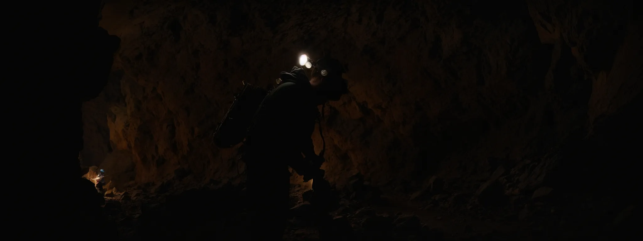 an image of a lone miner with a pickaxe and headlamp chipping away at a rock face deep in a dimly lit tunnel.