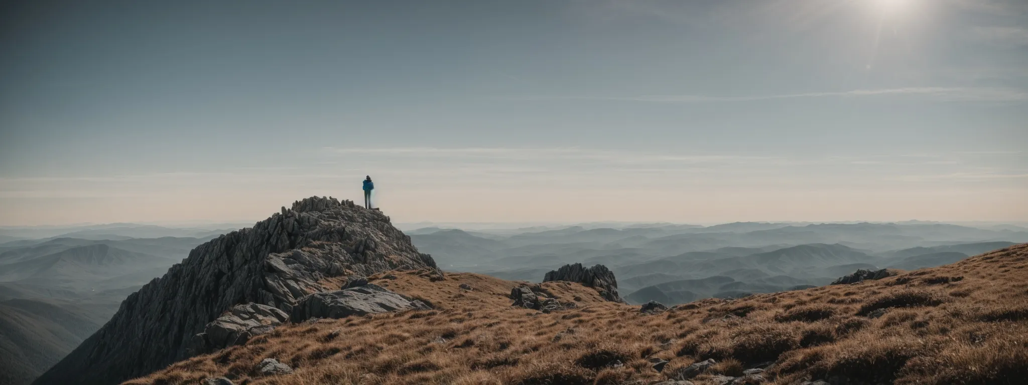 a hiker stands on a mountain summit, gazing out at a vast, untouched wilderness stretching into the horizon.