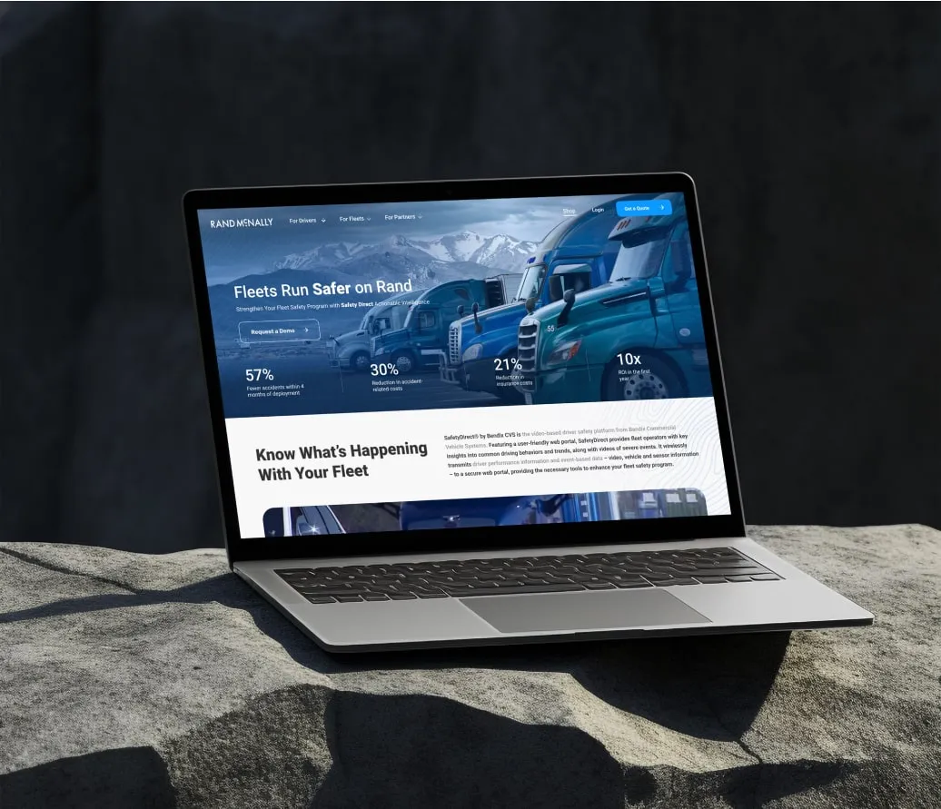 A laptop displaying a fleet management website with images of trucks and fleet statistics, placed on a large rock outdoors.