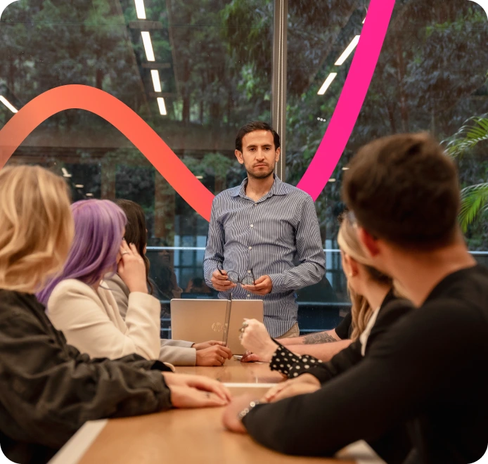 A man stands at the head of a conference table giving a presentation on Enterprise SEO Software to four seated colleagues in a modern office with large windows and a colorful wall graphic.